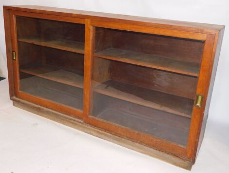 An early 20thC mahogany shop cabinet, with two glass fronted sliding doors, enclosing two shelves, raised on a plinth base, 99cm high, 182cm wide, 39cm deep.