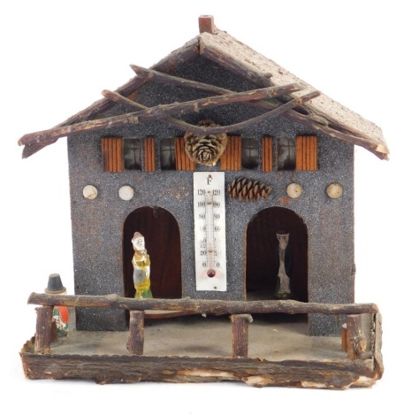 An early 20thC thermometer automaton, with articulated figures coming in and out of a house, with bark work front, 26cm high.