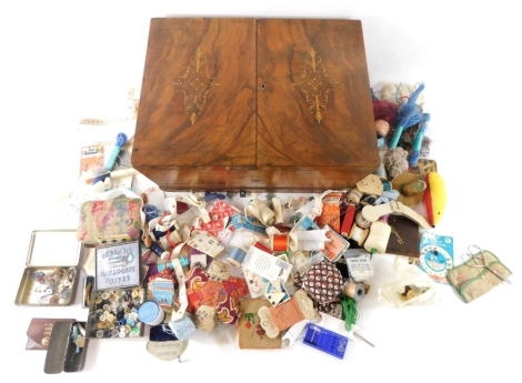 A Victorian walnut sewing box, hinging to the centre and revealing a fitted velvet lined interior, with floral inlay, and a quantity of various cotton, needles, and other sewing items, 17cm high, 42cm wide, 32cm deep.