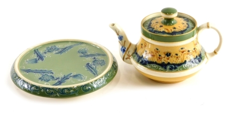 An early 20thC Macintyre pottery teapot, cover and similar stand, on green ground with yellow decoration, printed marks beneath, 16cm high.