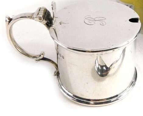 A George V silver mustard pot, by Edward Barnard and Sons Limited, of plain cylindrical form with thumb mould lid, ear shaped handle, and blue glass liner (initialled), London 1925, 6cm high, with associated spoon, 5.81oz all in.