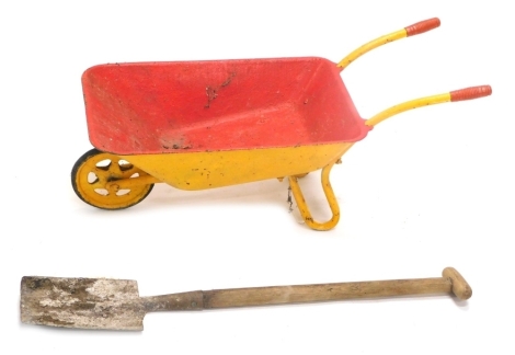 A child's metal wheelbarrow, painted yellow and red, with articulated front wheel and miniature spade, 75cm high. (2)