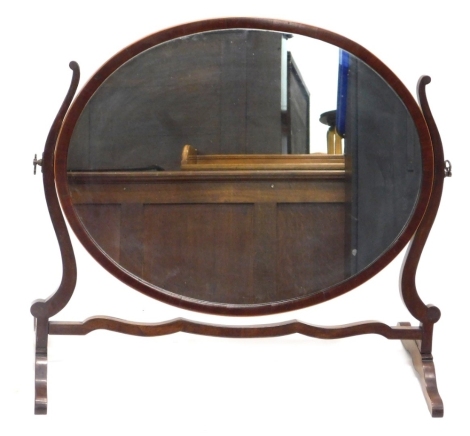 An Edwardian mahogany swing mirror, with oval frame on scroll feet, 66cm high, 75cm wide, 31cm deep.