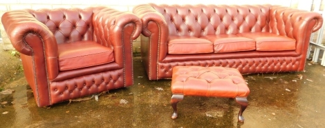 A three piece club style red leather lounge suite, comprising three seater Chesterfield settee and armchair, each in button back red leather, and similar footstool, the settee 69cm high, 198cm wide, 90cm deep.