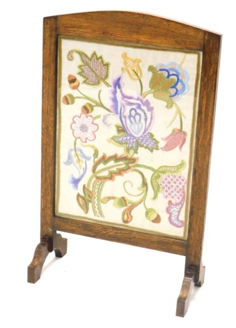 An early 20thC oak framed fire screen, with embroidered floral centre, on scroll feet, 75cm high, 43cm wide, 22cm deep.