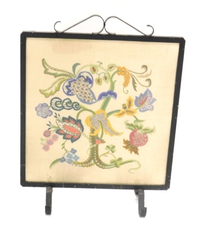 A 20thC iron framed fire screen, with floral embroidered centre, on scroll feet, 63cm high, 47cm wide, 19cm deep.