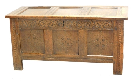 An 18thC oak coffer, the three panel top revealing a plain interior with candle box, the front carved with an arrangement of diamonds, on stiles, 57cm high, 114cm wide, 48cm deep.