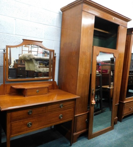 An Edwardian bedroom pair, comprising single door wardrobe with bevelled glass, flanked by oval panels, with drawer beneath, on bracket feet, and a mirror back dressing table, the shaped bevel glass flanked by urn topped plain supports, above a single dra