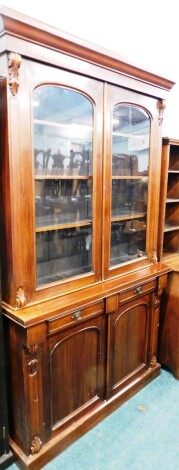 A Victorian mahogany library bookcase, the moulded cornice raised above acanthus leaf moulding, centred by a pair of dome topped glazed doors, revealing plain shelves, the subsection with two frieze drawers above a pair of panelled cupboards flanked by sc