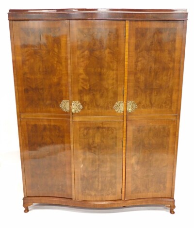 An Art Deco walnut and figured walnut serpentine fronted triple wardrobe, with pierced brass mounts, on short cabriole legs with pad feet, 193cm high, 51cm wide.