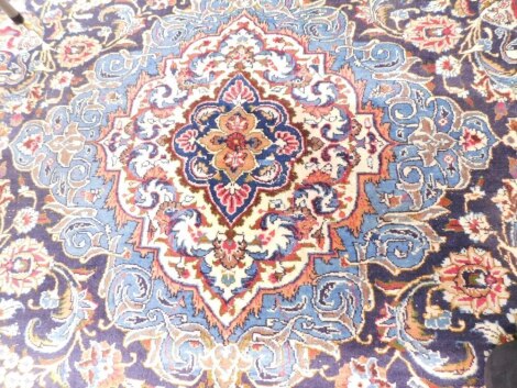 A Persian carpet, with a central medallion in cream and pale blue, surrounded by scrolls, vases, etc., mainly red on a navy ground with blue spandrels, one wide and three narrow borders, 387cm x 296cm.