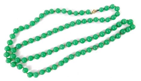 A string of jade coloured glass beads, on a knotted string strand, with yellow metal clasp, stamped 9ct, 90cm long, 109.1g all in.