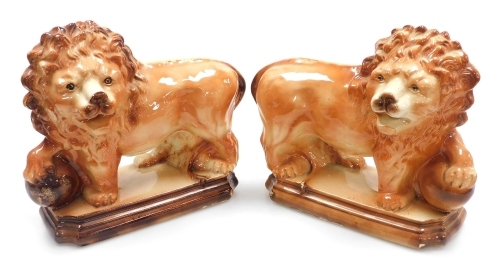 A pair of 19thC Scottish Bowness pottery lions, each modelled standing with a raised paw on a ball, on a stepped base, 29cm high.