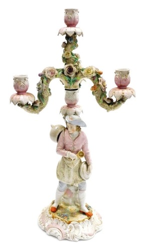 A late 19thC porcelain candelabrum, the candle arms modelled as tree branches with applied porcelain flowers, the central column modelled as a tree branch beside a gentleman holding a spoon and cooking pot, on a scroll base, gilt heightened, painted mark