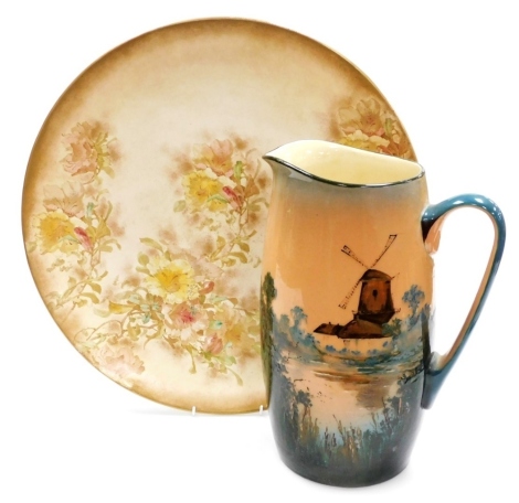 A late 19thC Royal Doulton Burslem blush porcelain charger, decorated with flowers, gilt heightened, printed marks, 44cm diameter, together with a Royal Doulton pottery wash jug, decorated with a windmill and lake scene, numbered D3594, printed marks, 31c