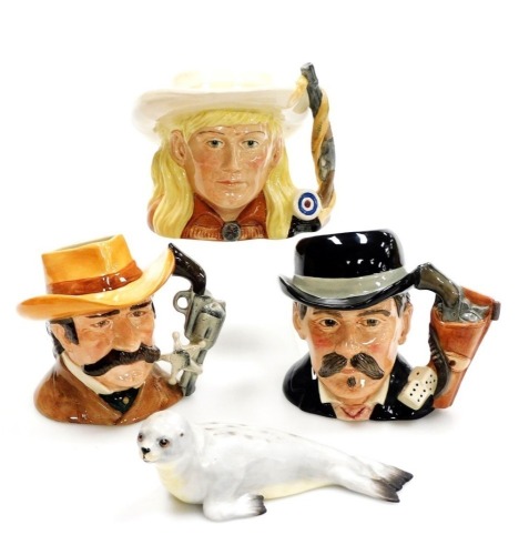 Three Royal Doulton pottery character jugs from the Wild West Collection, comprising Doc Holliday, D6731, Annie Oakley, D6732, and Wyatt Earp, D6711, together with an Aynsley matt porcelain model of a grey seal, 19cm wide. (4)