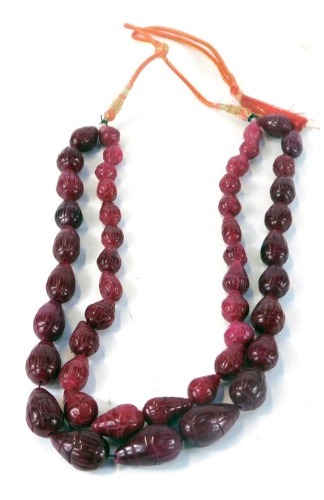 A reconstituted ruby two strand beaded necklace, with pear shaped carved beads, on a black string strand, with adjustable red and gilt cords, the rubies totalling approx 931.5cts overall, ruby section 44cm long, with adjustable cord, 194.4g all in.