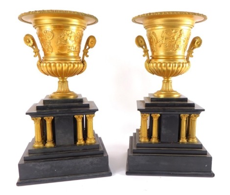 A pair of late 19thC gilt brass and slate garniture vases, the vases of semi fluted campana form, embossed with Roman warriors riding chariots, raised on a temple form plinth, supported by twelve composite capitols, raised on stepped rectangular bases, 33