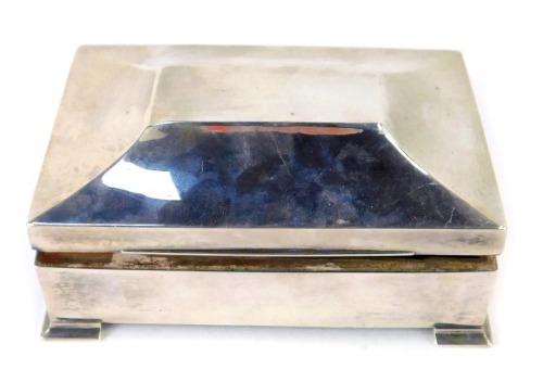 A George V silver cigarette box, with a shaped top, on out swept feet, bearing later engraving to reverse 'To My Friend BBH, Head Student N.T.C.D.J 1941-42 K.L.T', Birmingham 1911, with a wooden lined interior, 6cm high, 14cm wide, 15.99oz gross.