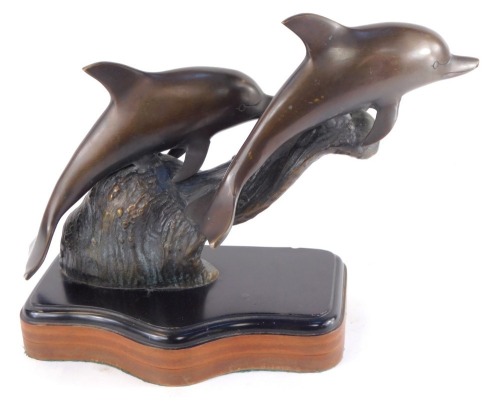 A bronze figure group of two dolphins, modelled riding the crest of a wave, raised on a serpentine mahogany and ebonised base, 36cm wide.