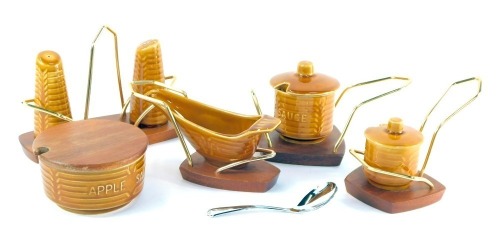 A Crown Devon treacle glazed pottery cruet set, comprising an apple sauce pot with wooden lid, mint sauce pot, sauce boat, salt, pepper, and mustard, printed marks, all on wooden stands.