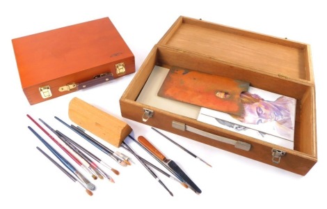 A Winsor and Newton beech artists paint box, 32cm wide, and a further artists paint box, containing brushes, pallet, and an example of the artist's work, 49cm wide. (2)