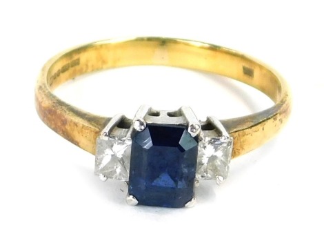 An 18ct gold sapphire and diamond dress ring, with a rectangular cut central sapphire, in a raised four claw basket setting, with two asscher cut diamonds, the diamonds totalling approx 0.25ct, in a white gold setting on a yellow metal band, ring size M½,