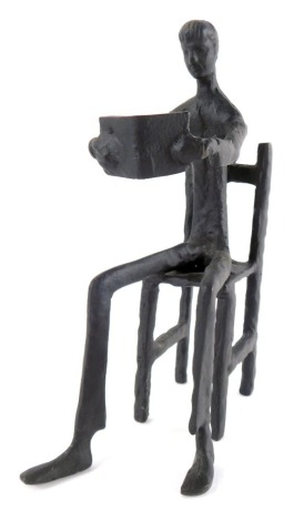 A mannerist cast iron sculpture of a man, modelled seated on a chair reading a book, 21cm high.