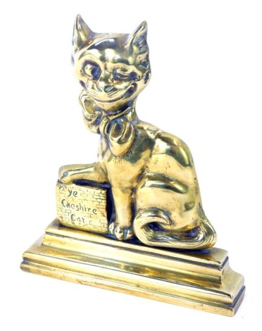 An early 20thC brass doorstop of 'Ye Cheshire Cat', modelled seated with his front paw resting on a titled wall, raised on a stepped base, 21.5cm wide.