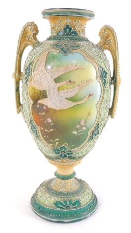 An early 20thC Noritake porcelain vase, of twin handled baluster form, decorated with reserves of swans in flight, and flowers, against a floral tube line decorated pale green ground, printed mark, 29cm high.