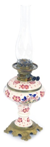 A 20thC ceramic oil lamp, on a white ground with pink flowers, on embossed brass base, with chimney, 59cm high.