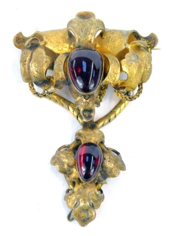 A Victorian gilt metal brooch, comprising one of heavy scroll decoration with cabachon red paste stone, 8cm wide, and an associated pendant/brooch section. (2)