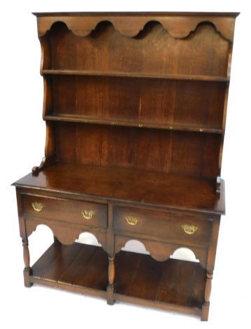 A 20thC oak dresser, with a moulded top above a two shelf plate rack, above two frieze drawers and shaped apron, raised on turned columns, united by an under tier, on stiles, 177cm high, 125cm wide, 50cm deep.