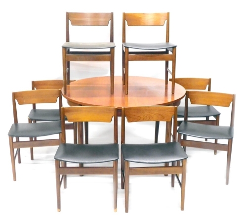 A 1960s/70s teak extending dining table, with integral leaf, on turned tapering legs, 120cm diameter enclosed, and a set of eight 1960s/70s teak dining chairs, each with a black padded seat, on turned legs. The upholstery in this lot does not comply with