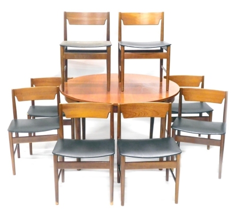 A 1960s/70s teak extending dining table, with integral leaf, on turned tapering legs, 120cm diameter enclosed, and a set of eight 1960s/70s teak dining chairs, each with a black padded seat, on turned legs. The upholstery in this lot does not comply with 