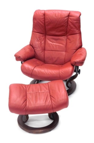 A Stressless style red leather swivel armchair, on shaped supports, and a matching stool.