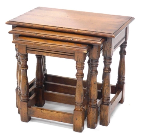 A nest of three oak Titchmarsh and Goodwin style tables, with baluster stems and block stiles, the largest 49cm high, 58cm wide, 35cm deep.