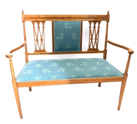 An early 20thC salon settee with urn finials upholstered back, flanked by lattice splats with an overtstuffed seat in floral material, with scrolls arms, turned supports and square tapering legs, 101cm high, 106 wide, 49cm deep.