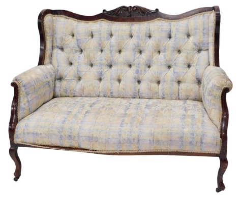 A 20thC walnut salon settee, the serpentine back centrally carved with bell flowers, scrolls and acanthus leaves, with an overstuffed button back, arms, and serpentine seat, in later floral material, on cabriole front and sabre back legs terminating in ca