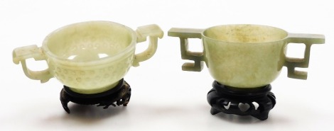 Two Chinese jade libation cups, each carved with ring handles, 4cm high and 3.7cm high, with carved wooden stands.