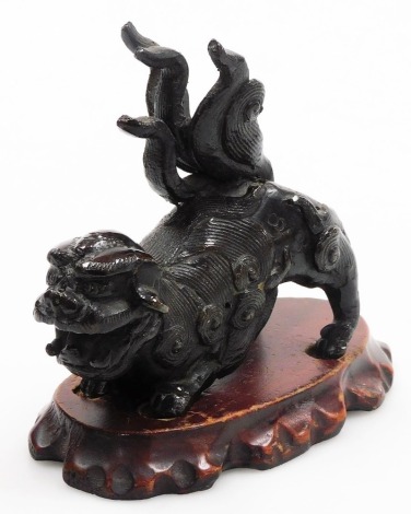 A late 19thC Chinese bronze Buddhistic lion, in crouching pose, with wooden stand, 11cm high overall, 13cm long.