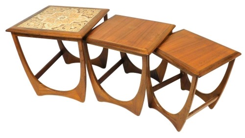 A nest of three mid 20thC teak tables, the largest with a tiled top, each raised on U shaped solid supports, the largest 50cm high, the top 50cm x 50cm.