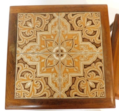 A nest of three mid 20thC teak tables, the largest with a tiled top, each raised on U shaped solid supports, the largest 50cm high, the top 50cm x 50cm. - 2