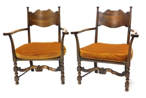 A pair of early 20thC Arts and Crafts style walnut open armchairs, each with a solid splat, shaped arms and a loose cushion with scroll shaped stretcher.