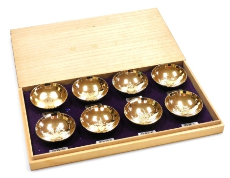 A set of eight gold plated Japanese sake bowls, depicting each of the Seven Lucky Gods (shichifukujin) and one with the characters reading shichifukujin, stamped to underside 24k GP, each 6.5cm diameter, in a fitted box, the box 33.5cm wide.