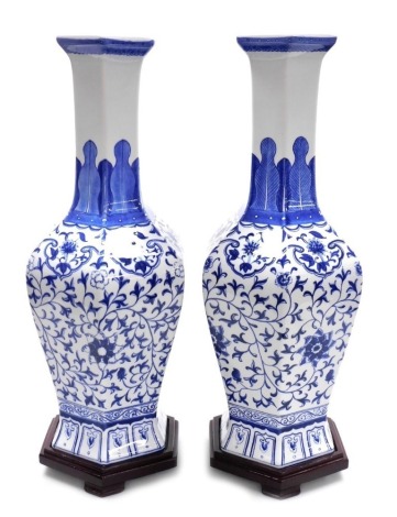 A pair of Chinese 20thC blue and white vases, of hexagonal, slender necked form, decorated with scrolling lotus flowers, beneath a band of stylised leaves, with wooden stands, 58.5cm high.