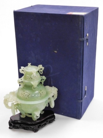 A 20thC Chinese green jade censer and cover, the pierced cover with eight flower head ring finials, the base with two pierced floral handles with two large rings, above four further small rings, raised on four feet, on a hardwood base, 27cm high overall, 