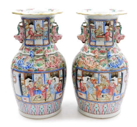 A pair of 19thC Cantonese famille rose vases, of baluster form, with an elongated neck and dog of fo moulded handles, each decorated with reserves of figures in interior scenes against a floral background, with applied moulded dragons, gilt heightened, ea