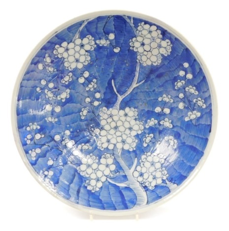 A Japanese blue and white porcelain charger, decorated with prunus blossom against a scale ground, restored, 38cm diameter.