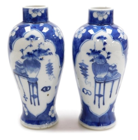 A pair of early 20thC Chinese blue and white baluster vases, decorated with reserves of interior objects against a blue ground decorated with prunus blossom, under glaze blue four character Kangxi mark, 18.5cm high.